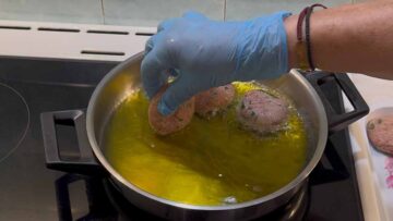 Ένα χέρι ρίχνει κεφτέδες σε τηγάνι με ελαιόλαδο.