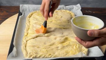 Ένα χέρι ρίχνει λιωμένο βούτυρο πάνω από το φύλλο.